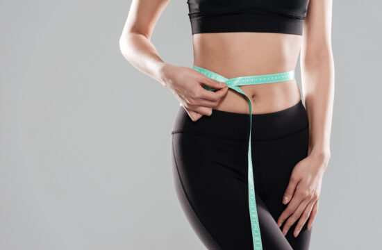graphicstock closeup of woman athlete standing and using measuring tape on her waist over gray background rdlU8WAIhl