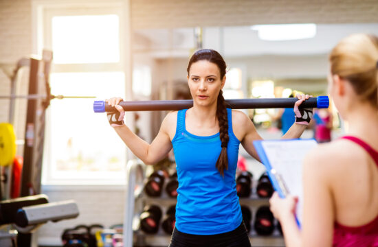 graphicstock woman in blue singlet exercising with bar in a gym with her personal trainer writing into exercise plan on clipboard S IiDMBG