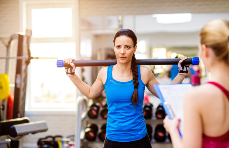 graphicstock woman in blue singlet exercising with bar in a gym with her personal trainer writing into exercise plan on clipboard S IiDMBG