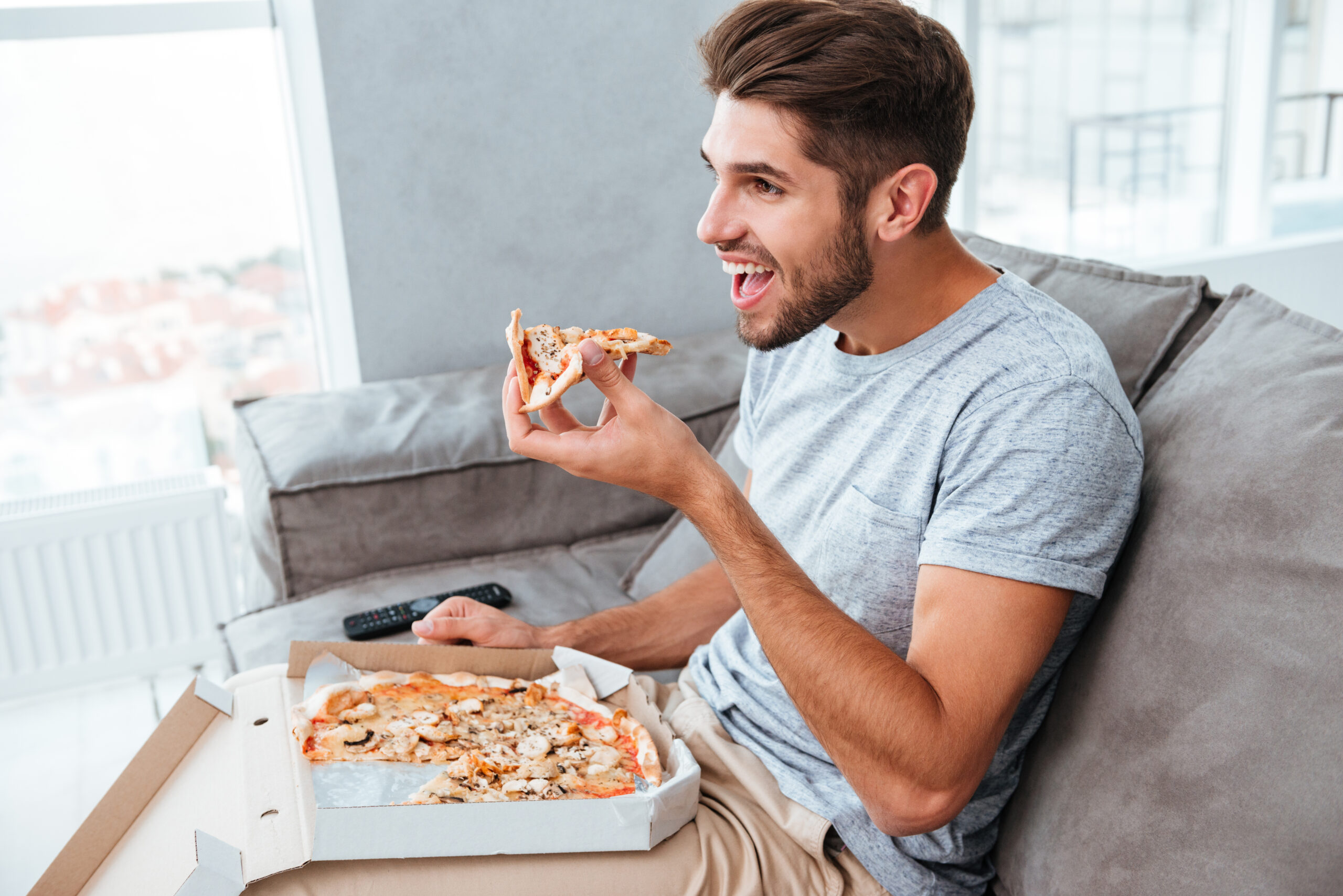 5 Common Mistakes People Make When Starting a New Diet 2 graphicstock picture of cheerful hangry young man eating pizza while sitting on sofa and watching tv BuqqjnSnx scaled